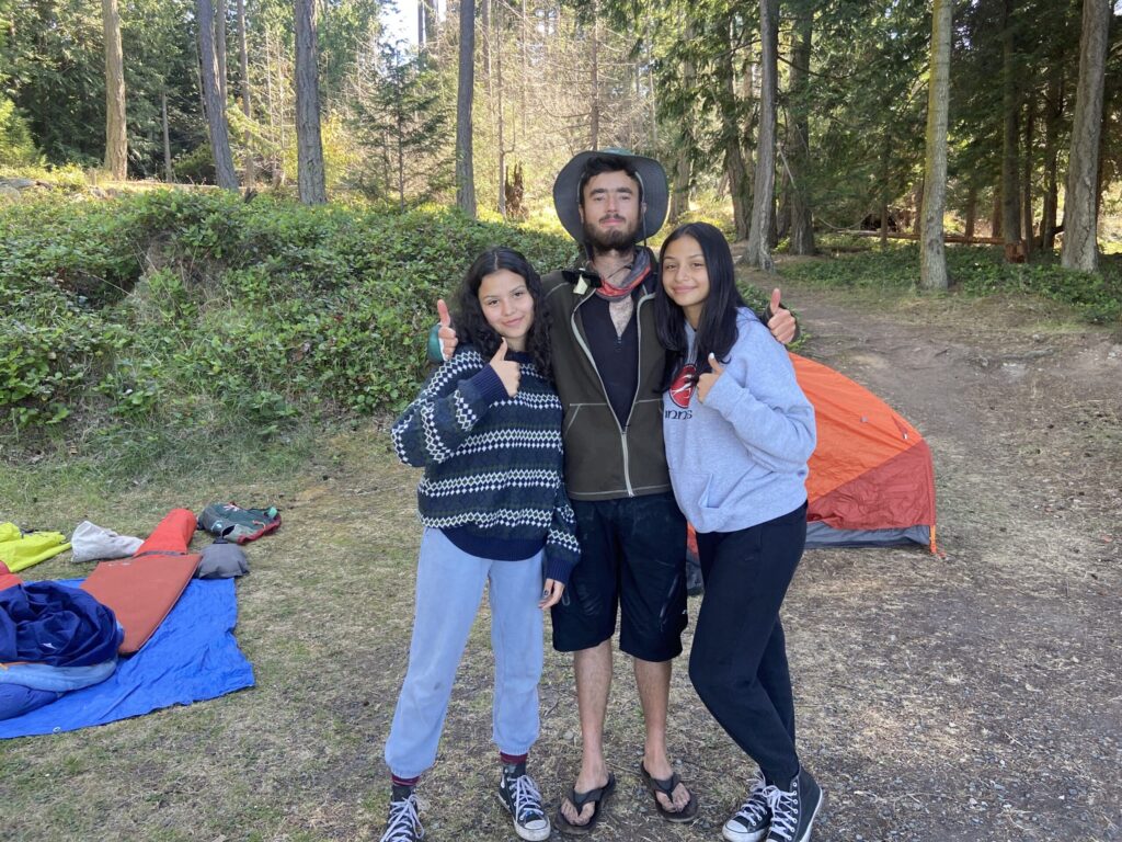 Three people at a campsite giving thumbs up