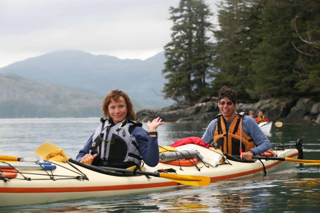 An advenurous couple kayaking in Alaska waves to you