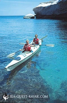 Two people kayaking on clear blue water near a rocky coastline